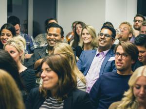 groupof people sitting in an audience and laughing, smiling, and engaging with the speaker. 