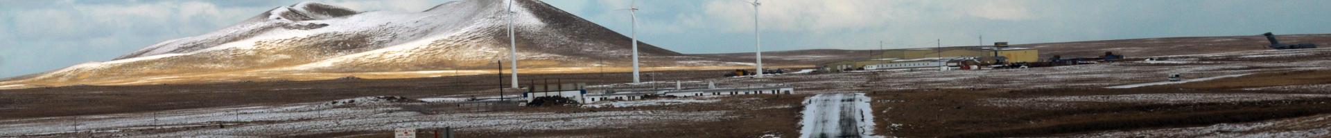 Icy road leading into a small town with snoq capped mountains and three windmills in the background
