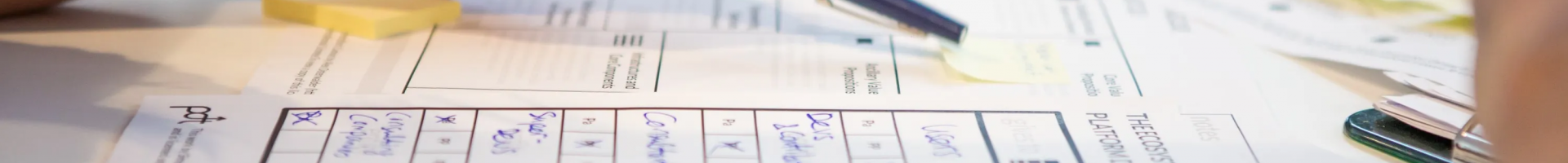 Zoomed in view of someone preparing a report. Someone is reaching across the papers with a pen.