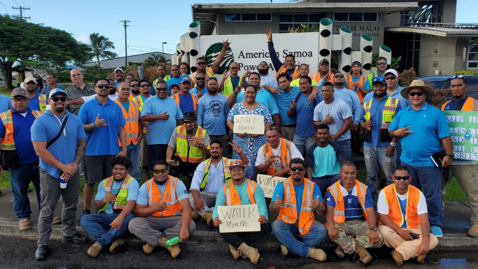 A group photo of about 30 people smiling at the camera; some of them are cheerfully holding up signs that read "Water Month"