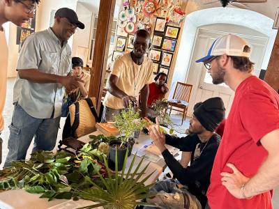 A small group of people gathering around a table with a professional guiding students as they interact and learn about plants, using live specimens.