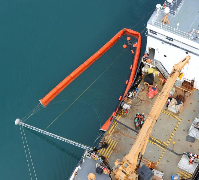 Ship with inflatable boom unfolding over water