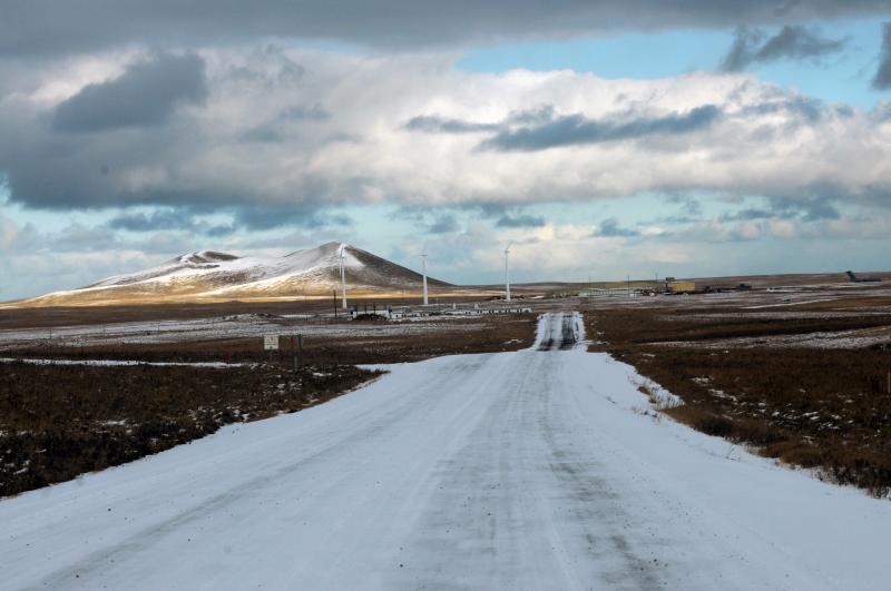 Icy road leading into a small town with snoq capped mountains and three windmills in the background