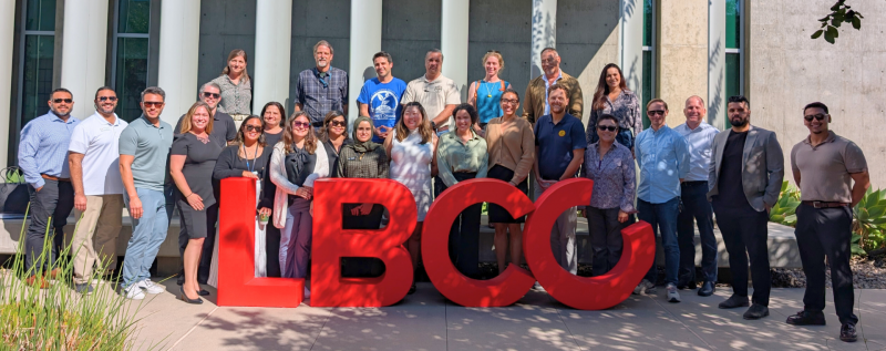 A large group of people gathered around large red "LBCC" letters on a sunny day
