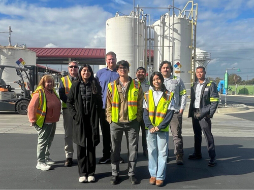 A group photo in front of large industrial towers on a sunny day.