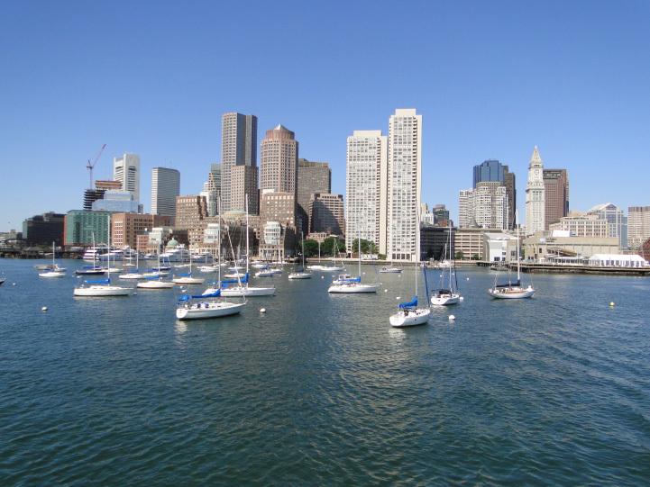 A city skyline with a large body of water in front of the buildings and boats at anchor.