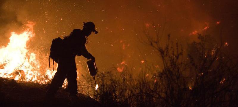 Silhouette of fire crew member against backdrop of fire and smoke