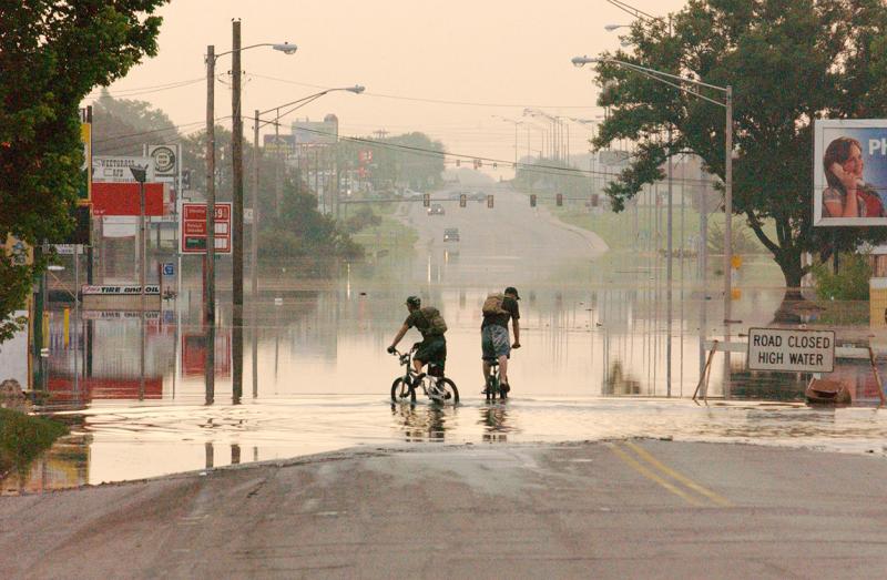 People riding bicycles through a flooded street in Miami, OK