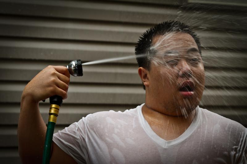 A man spraying himself with a garden hose during a heat wave