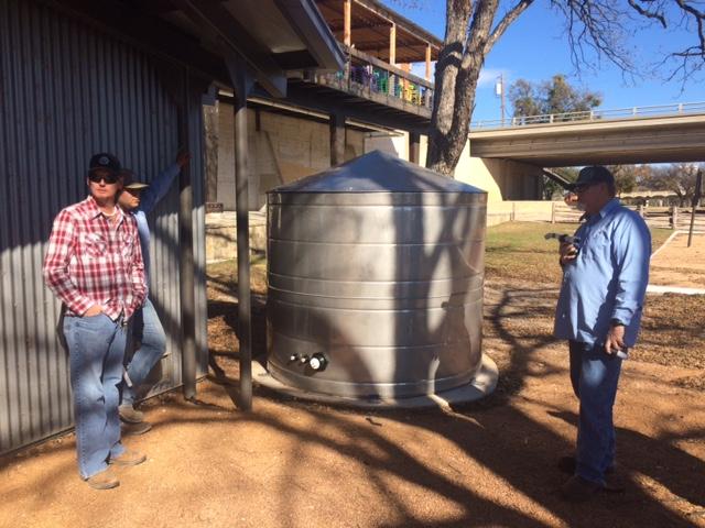 Three men standing next to a rainwater harvesting system
