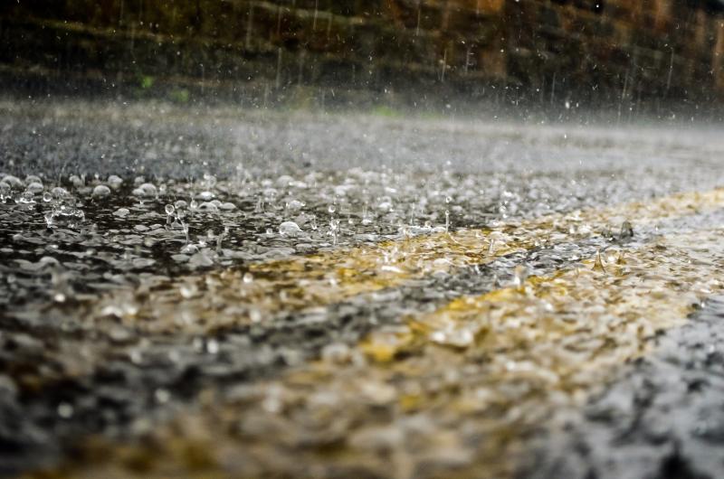 Rain falling on an asphalt road with a double-strip of yellow running through the middle.