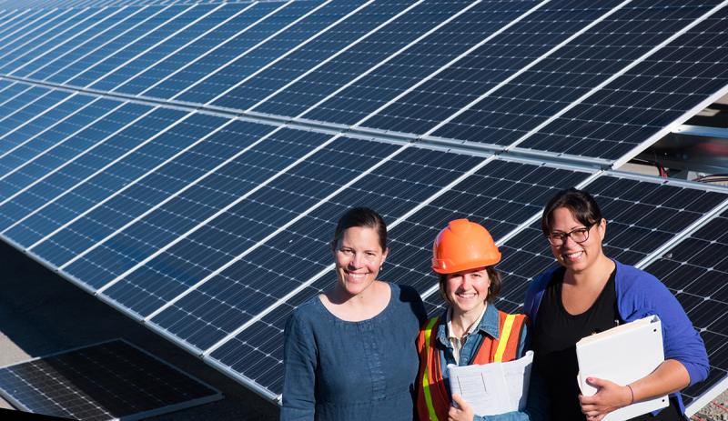 Three women standing in front of an installed solar grid