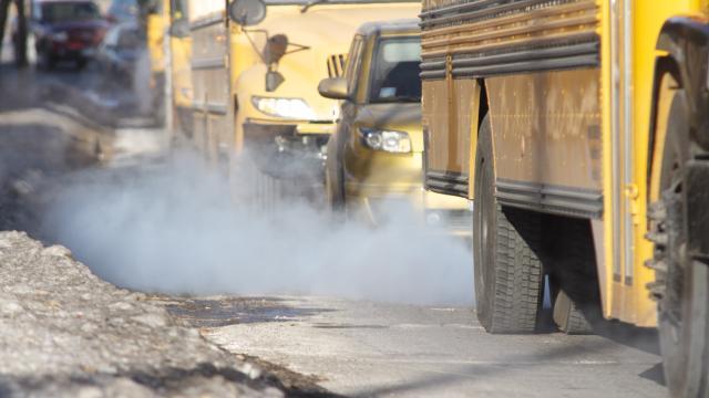 School buses and cars in traffic with exhaust visibly escaping their vehicles