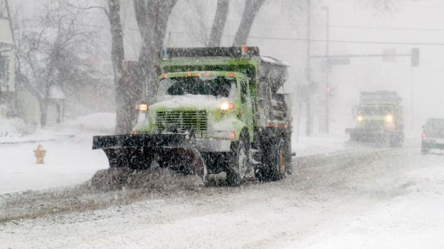 Snow plow going down a street that is covered in snow